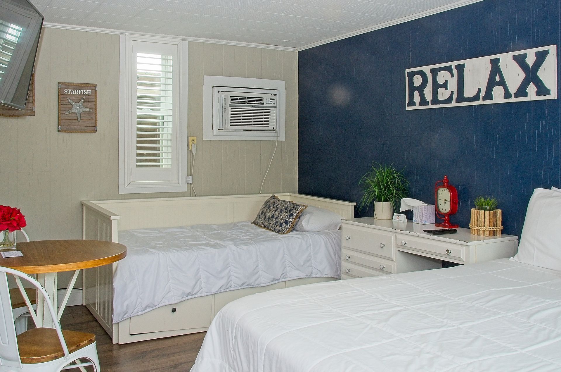 Hotel room with two beds, a small table, and a daybed; navy blue accent wall with a