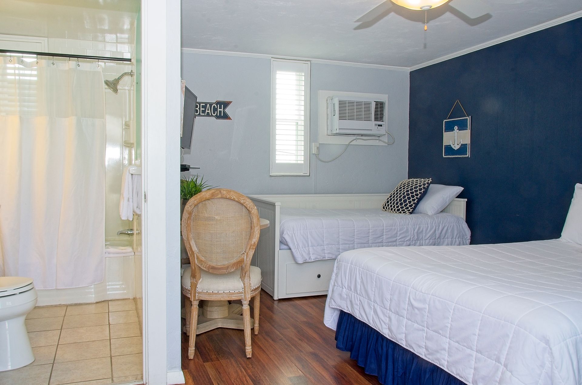 A hotel room with a queen bed, a daybed, and a bathroom visible on the left. The walls are blue and white.