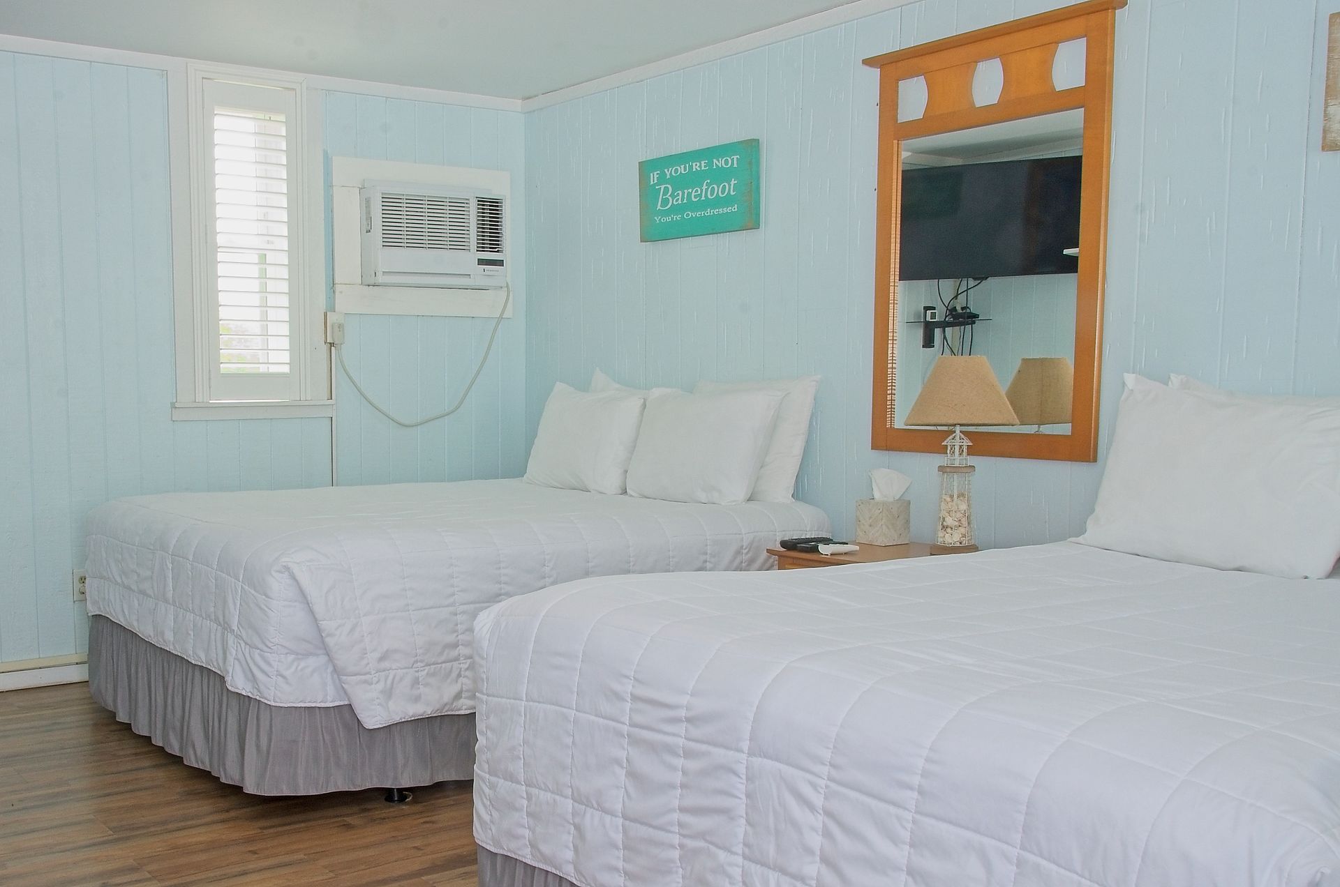 A motel room with two queen beds, white linens, light blue walls, and a window air conditioner.