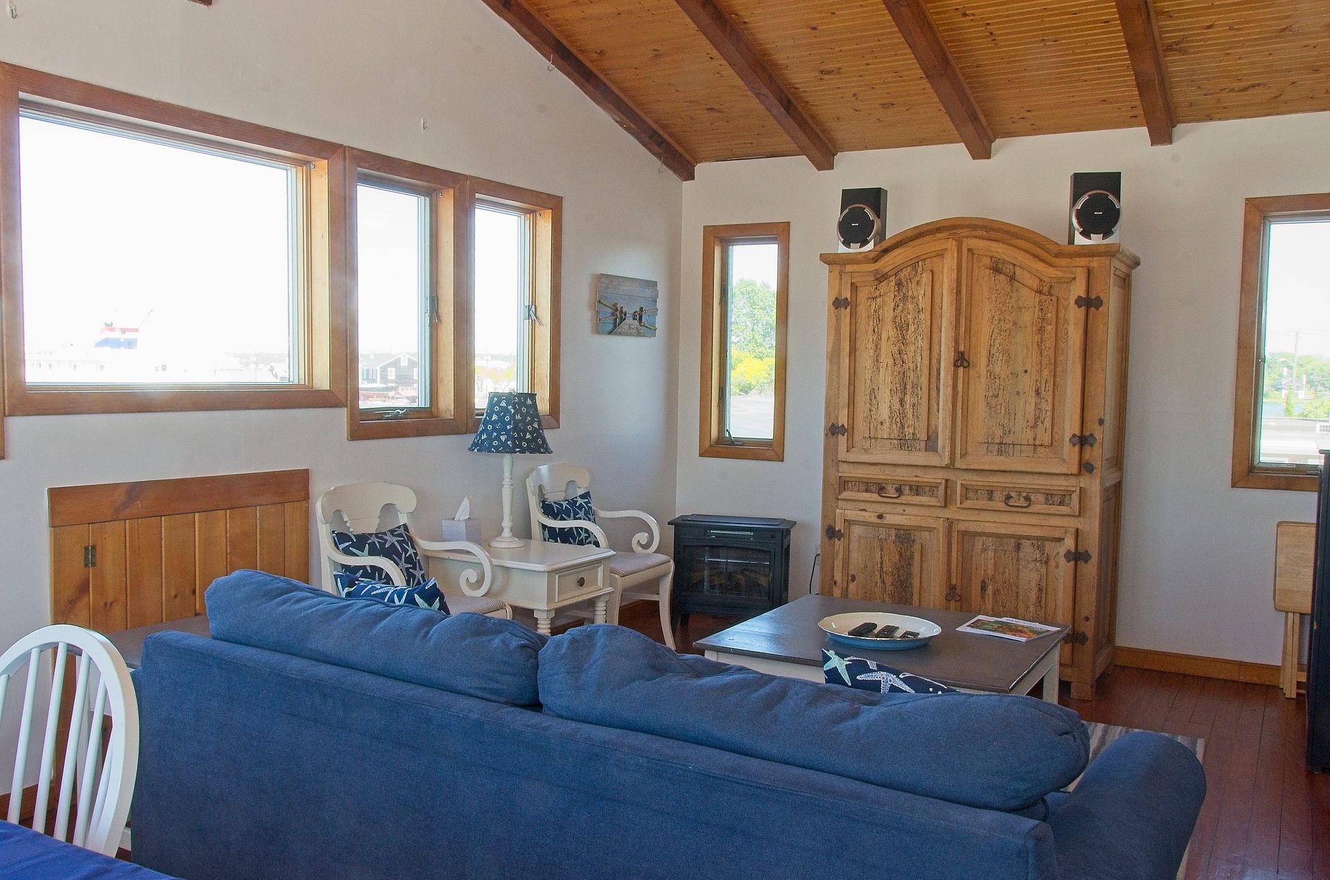 A cozy living room with a blue sofa, wooden cabinets, and large windows with ocean views.
