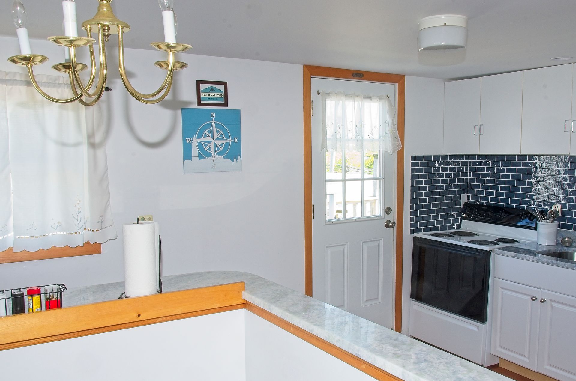 Interior view of a small kitchen with white cabinets, a stove, and a half wall with a counter. A door leads outside.