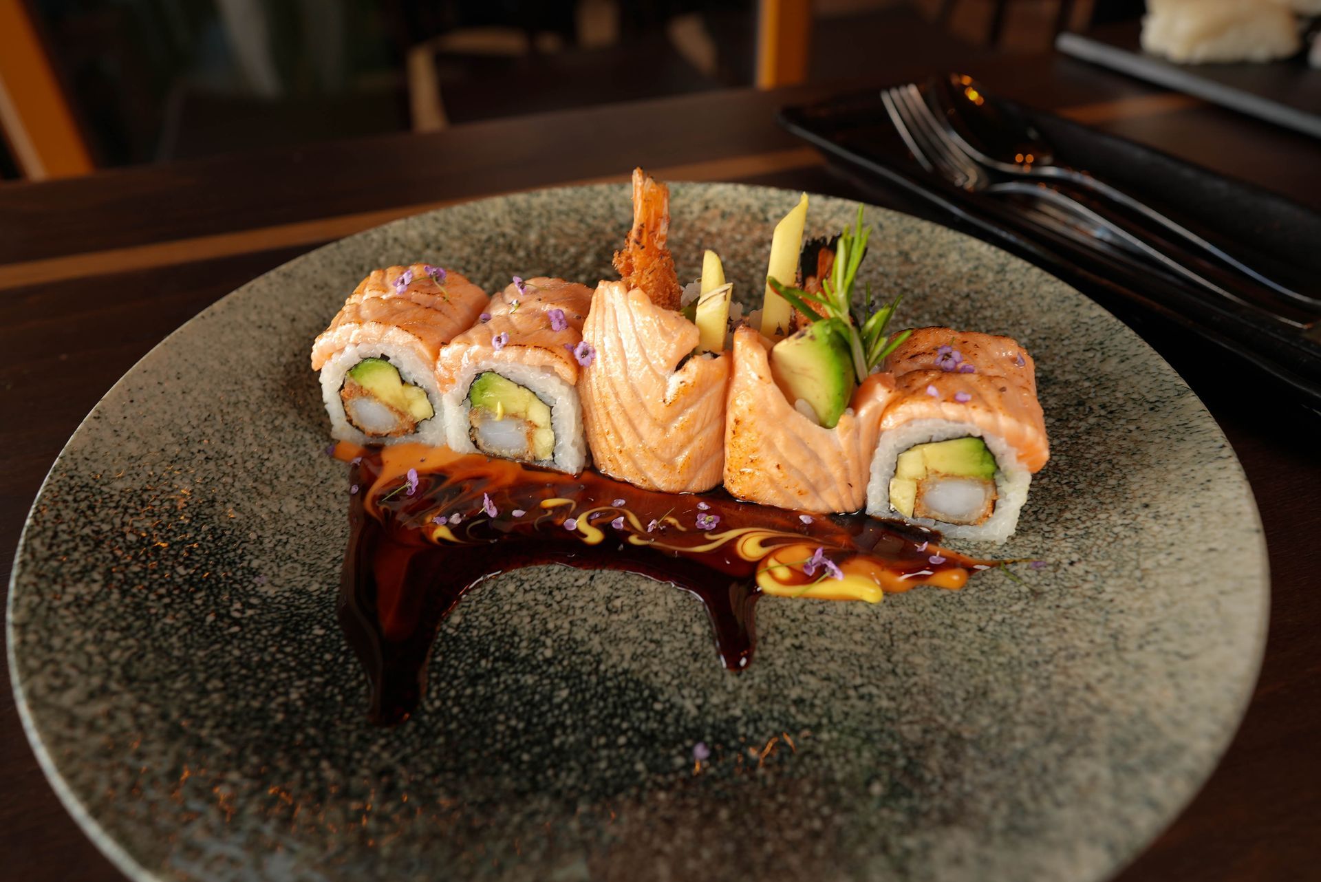 Sushi-Rollen und Nigiri auf einem dunklen Teller mit Sojasauce beträufelt auf einem Restauranttisch