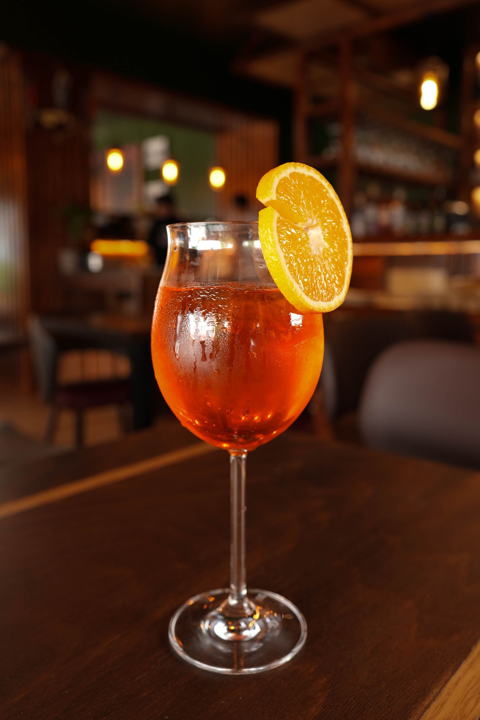 Orangencocktail in einem Stielglas mit einer Orangenscheibe als Garnitur auf einem Bartisch