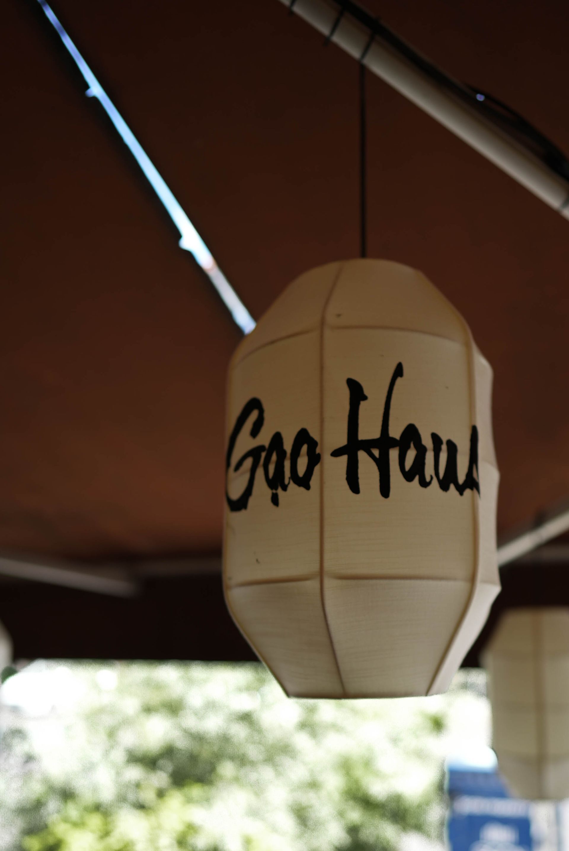 Weiße Hängelaterne mit der Aufschrift „Gao Hwa“ unter einem braunen Baldachin im Freien