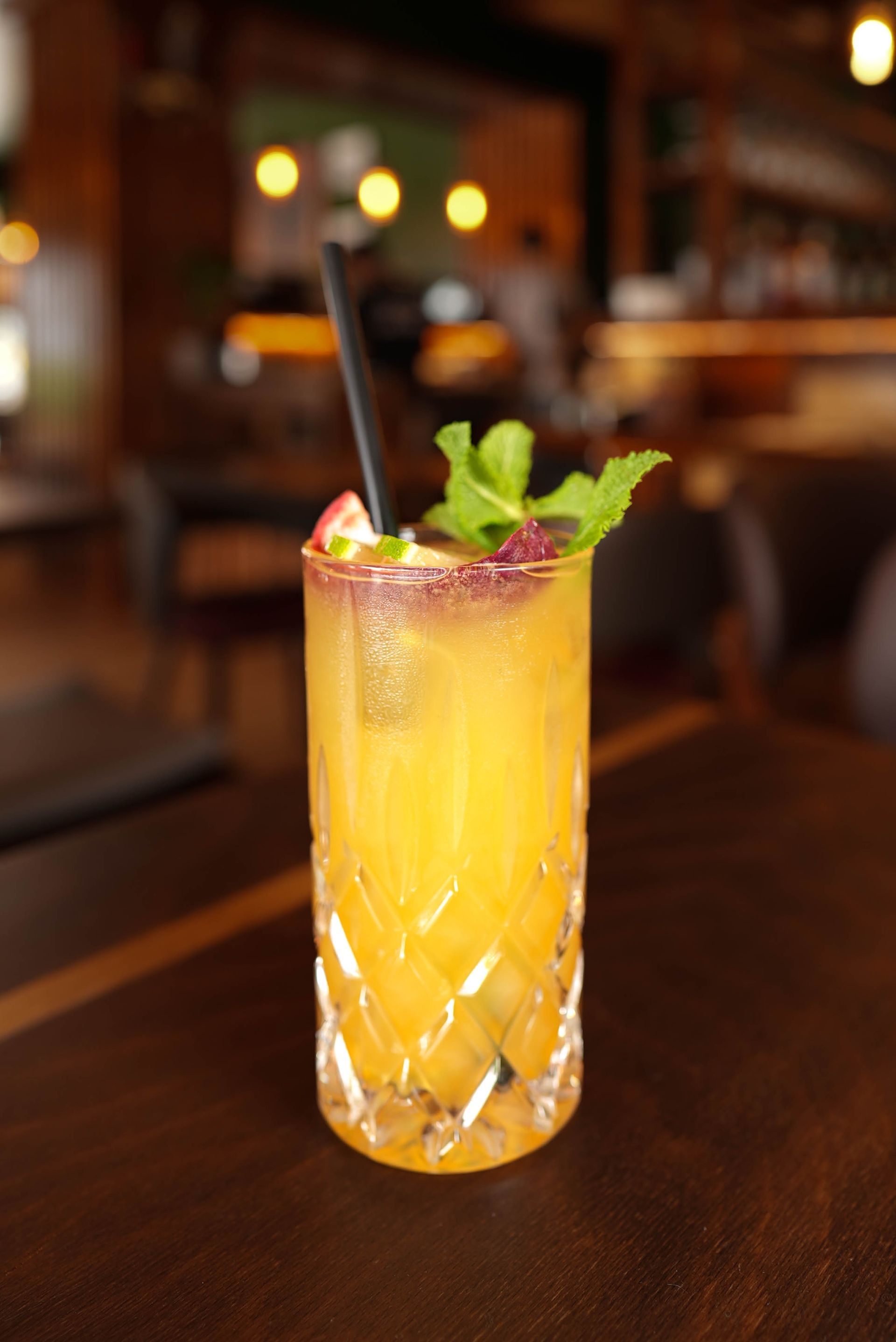 Ein hoher Orangencocktail mit Minze und Strohhalm auf einem Bartisch in einem schwach beleuchteten Restaurant