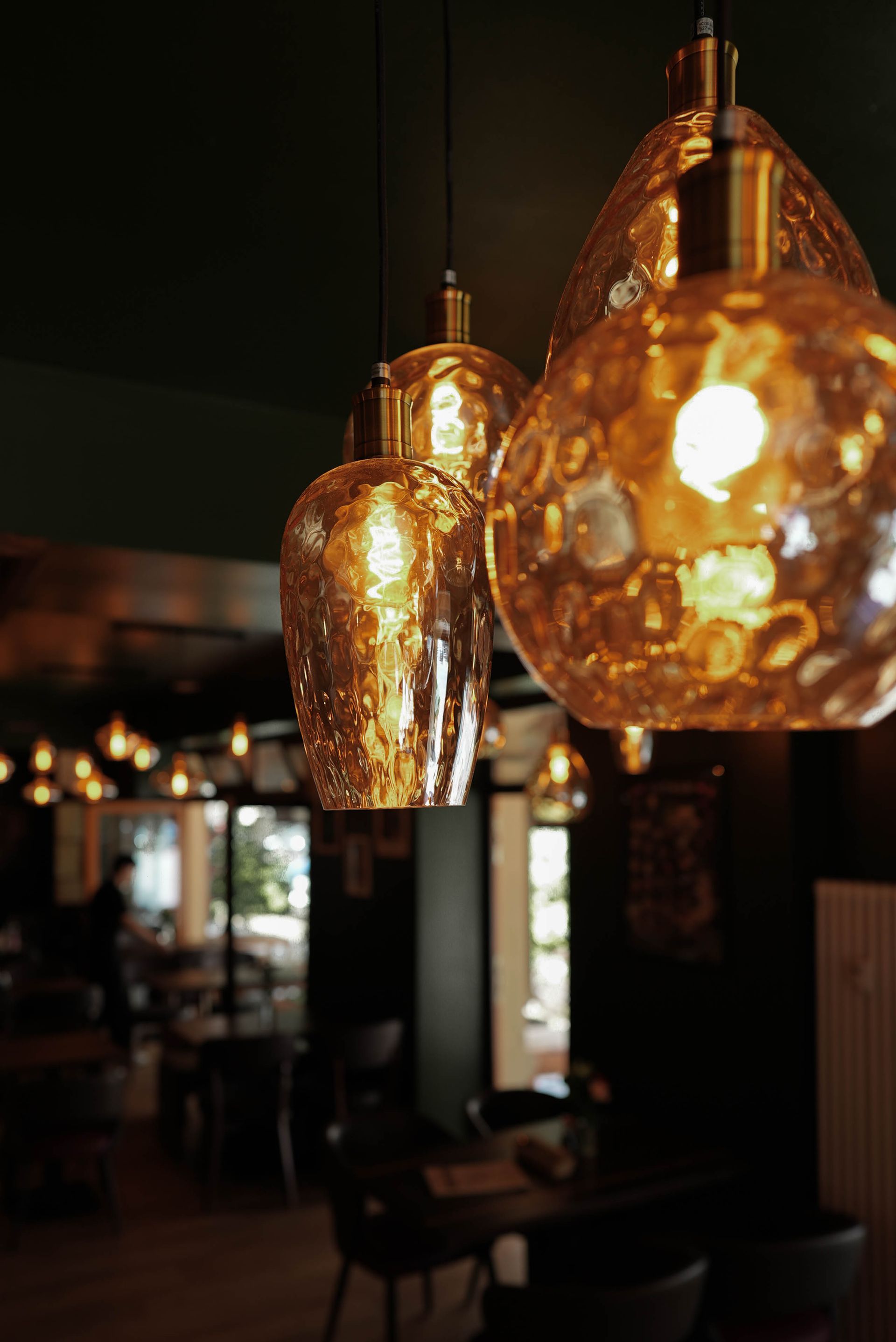 Warme, bernsteinfarbene Pendelleuchten hängen über dem schwach beleuchteten Interieur eines Restaurants oder einer Bar.