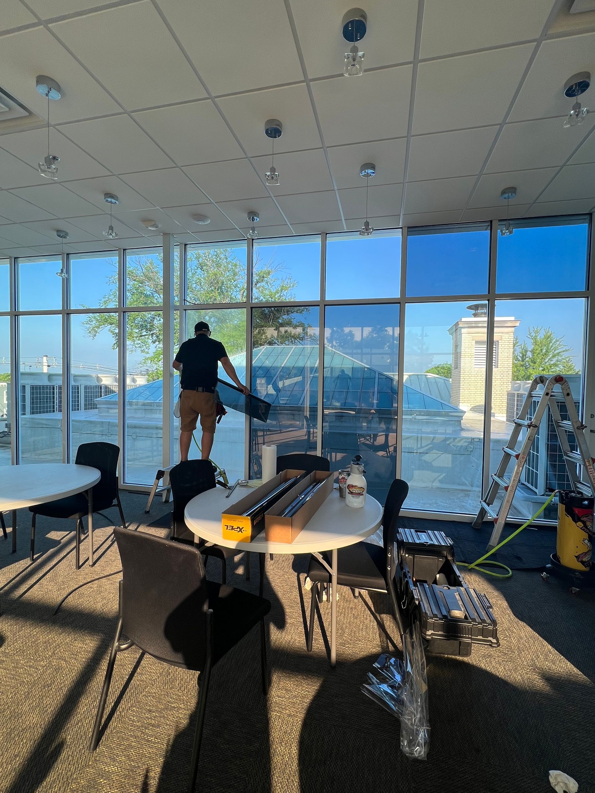 A person applying window tinting film to large glass panes in a brightly lit, modern commercial office space.
