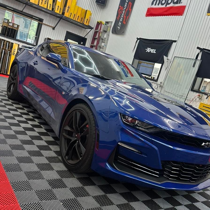 A dark blue Chevrolet Camaro parked inside a garage with black-and-white checkered flooring and automotive branding.
