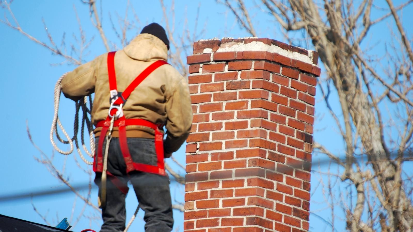 A man is standing on top of a brick chimney.