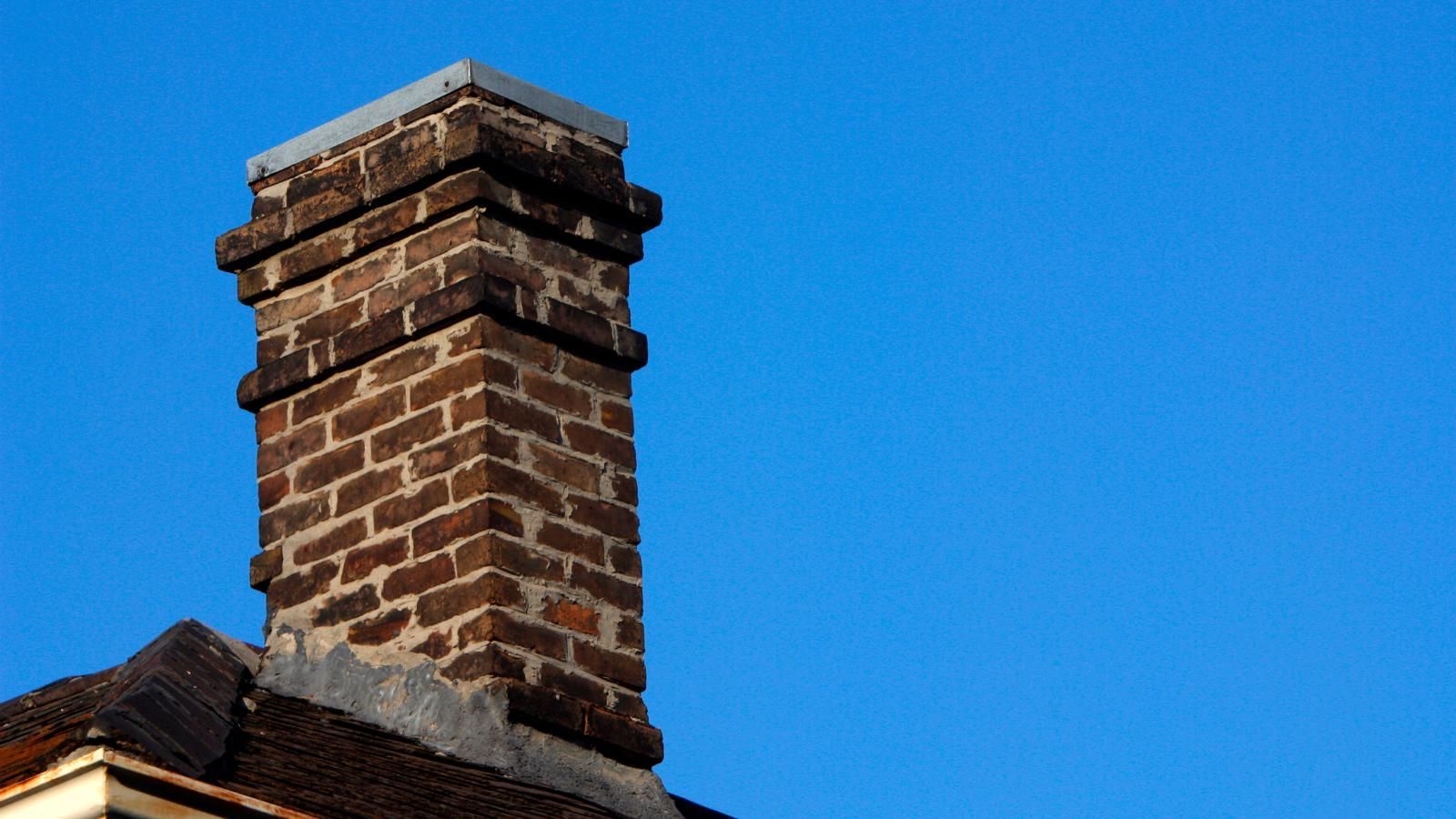 Brick chimney against a clear blue sky; a rooftop is visible at the bottom.
