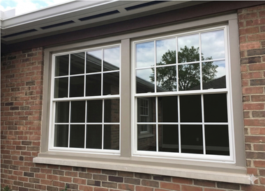 A double-hung window with a white grid frame, set into a red brick wall with a concrete sill.