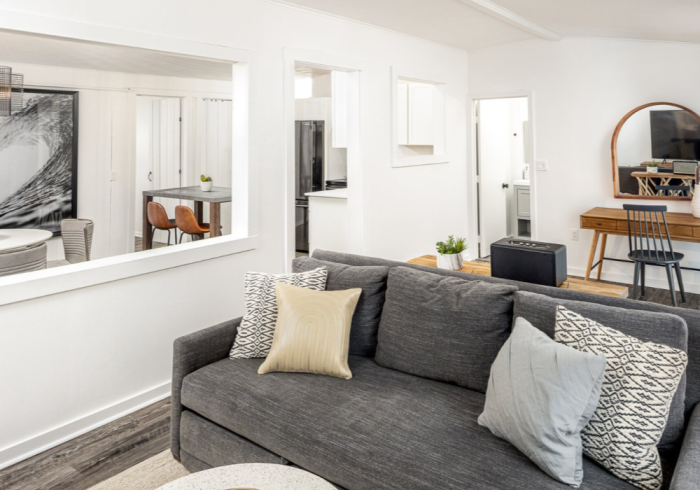 Living room with gray sofa, pillows, and wooden desk. White walls and large mirror.