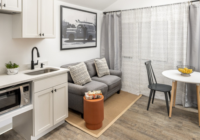 Small studio apartment with kitchenette, gray sofa, small dining area, and artwork.