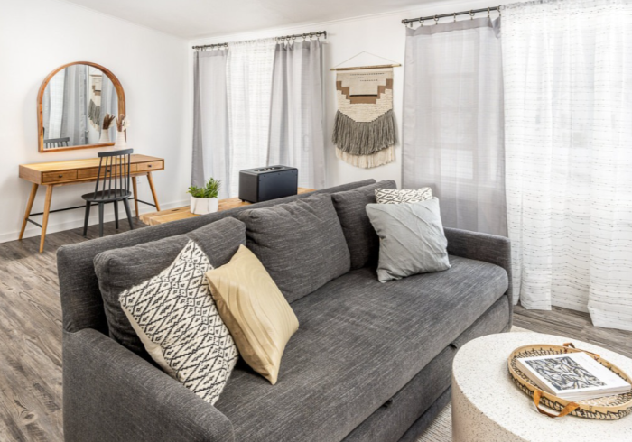 Gray couch with decorative pillows in a modern living room setting; desk and curtains.