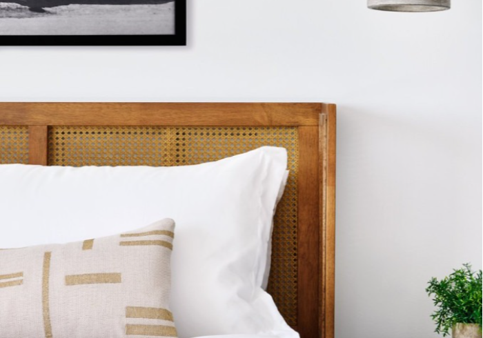 Wooden headboard with woven cane panel, white bedding and decorative pillows in a bedroom setting.