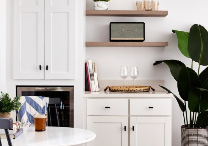 White kitchen with cabinets, open shelves, potted plant, and a table with a drink.