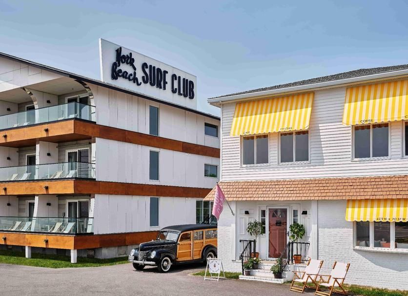 Jack Beach Surf Club, two buildings, one with a sign. Wooden station wagon parked in front of one. Yellow awnings.