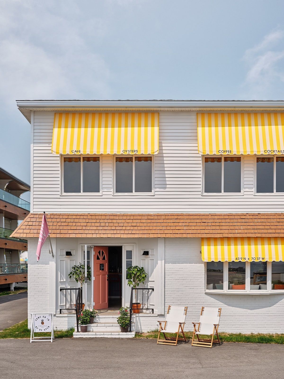 Two-story building with white exterior, yellow striped awnings, and pink door.
