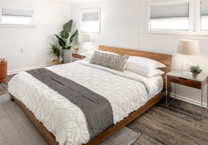 Modern bedroom with a wooden bed, white bedding, and gray accents.