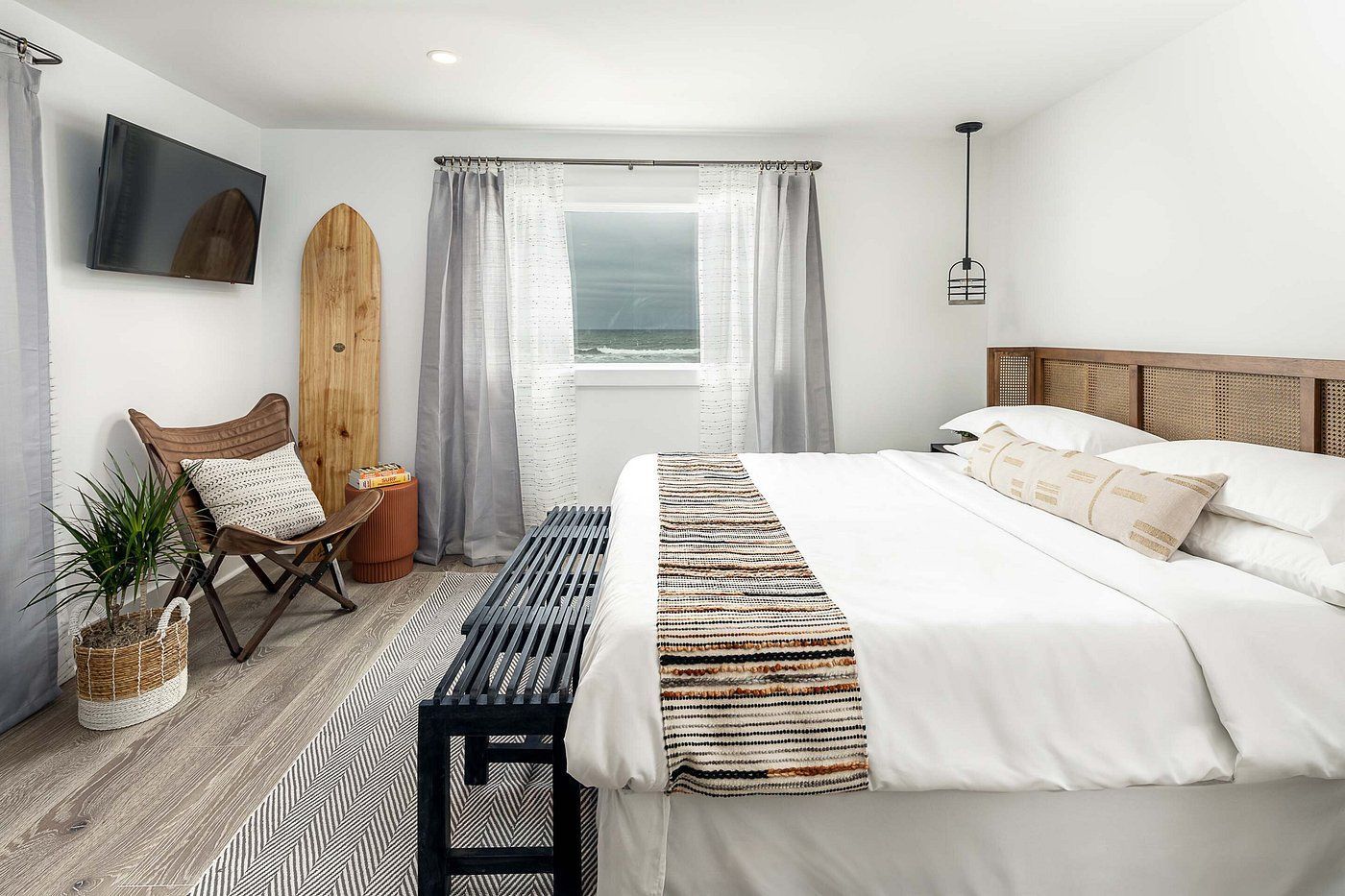 Bedroom with white walls, king bed, wooden headboard, surfboard, and armchair.