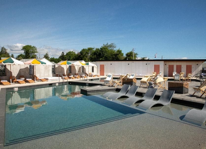 Poolside scene with a rectangular pool, lounge chairs, and cabanas under a blue sky.