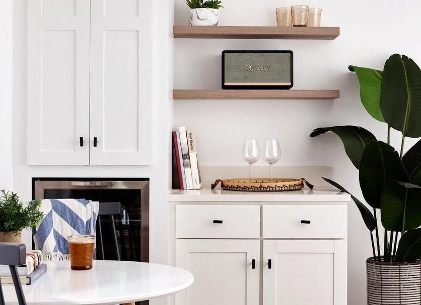 White kitchen with cabinets, open shelves, wine glasses, and a potted plant.