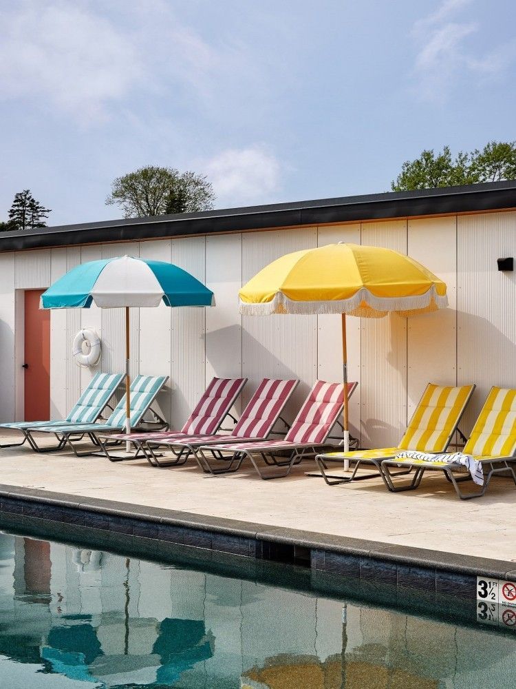 Poolside scene with striped lounge chairs, colorful umbrellas, and a blue pool.