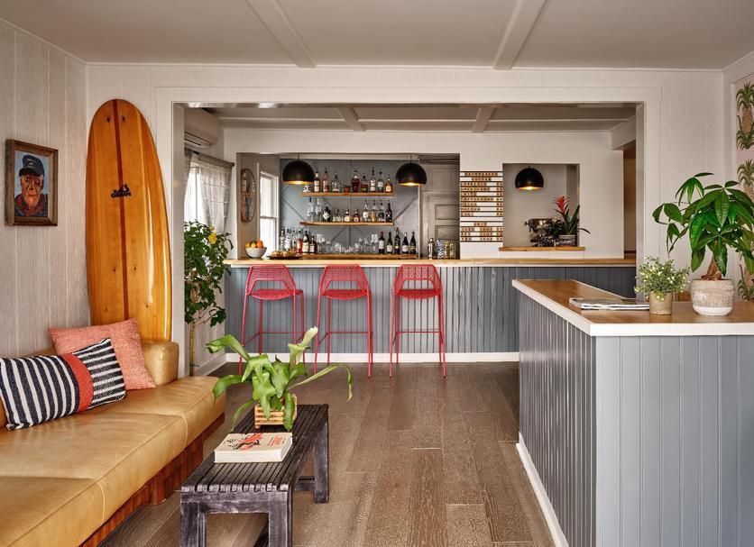 Interior with a bar, seating, and surfboard; wood floors and gray walls; red bar stools.