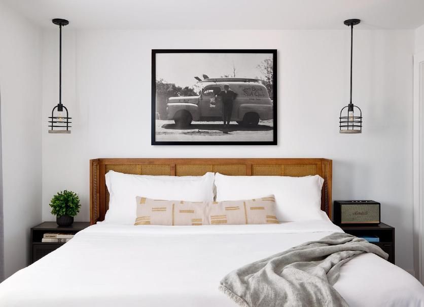 Bedroom with large bed, wooden headboard, black framed artwork, and hanging pendant lights.