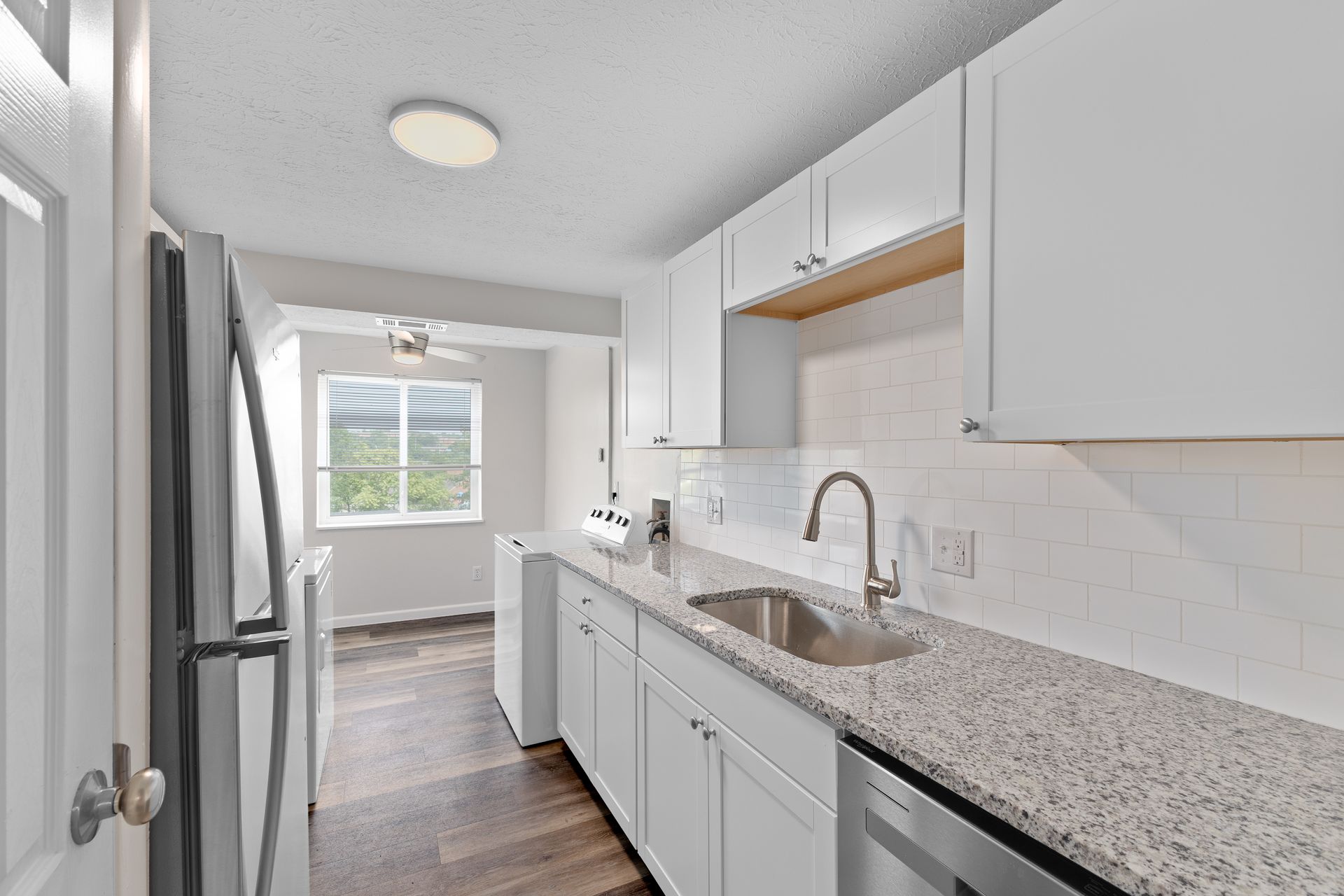 Modern kitchen with white cabinets, granite countertops, stainless steel appliances, and wood-style flooring.”
