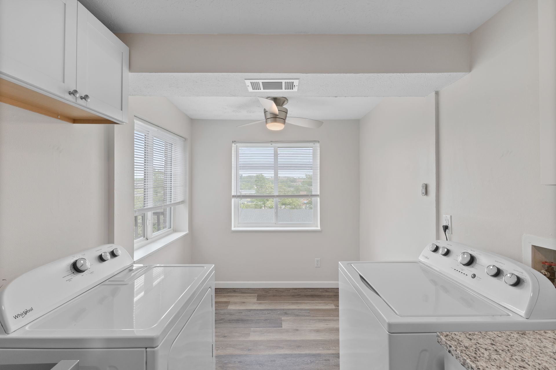 Laundry room with full-size washer and dryer, storage cabinets, and window for natural light.