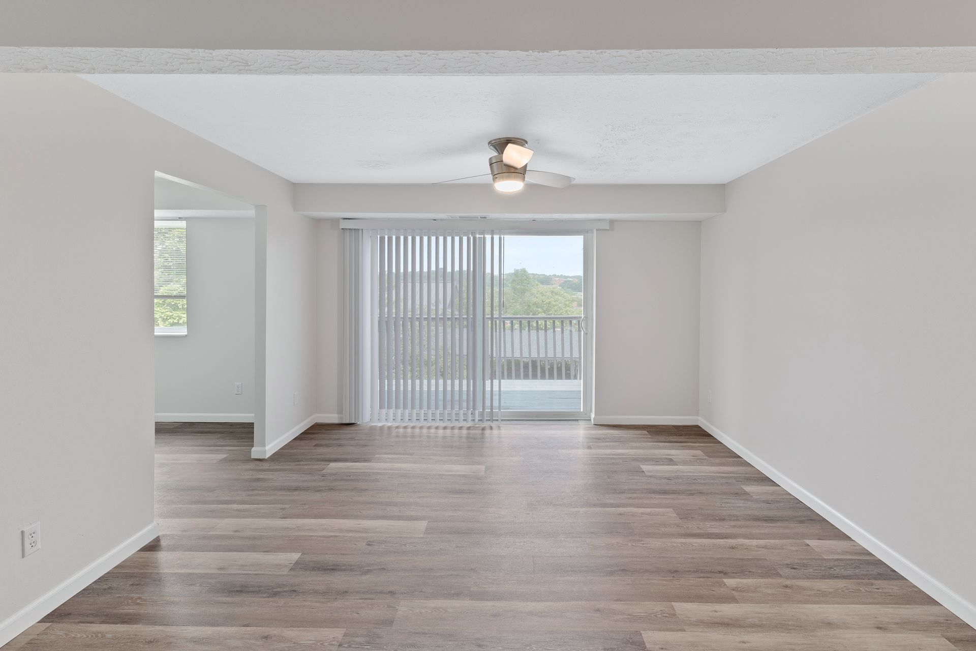 Open apartment living room with ceiling fan, sliding glass doors, and wood-style flooring.