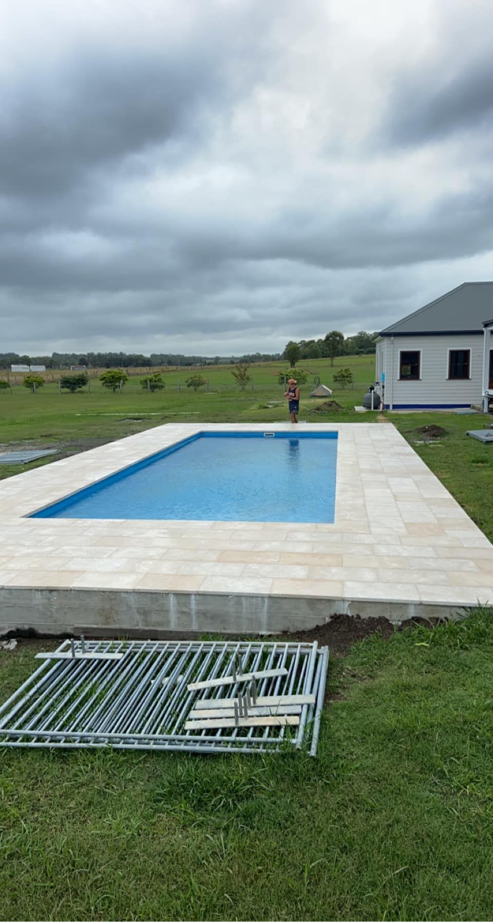 Rectangular pool with blue water and beige tile surround, overcast sky, residential backyard. — East Coast Paving in Seaham, NSW