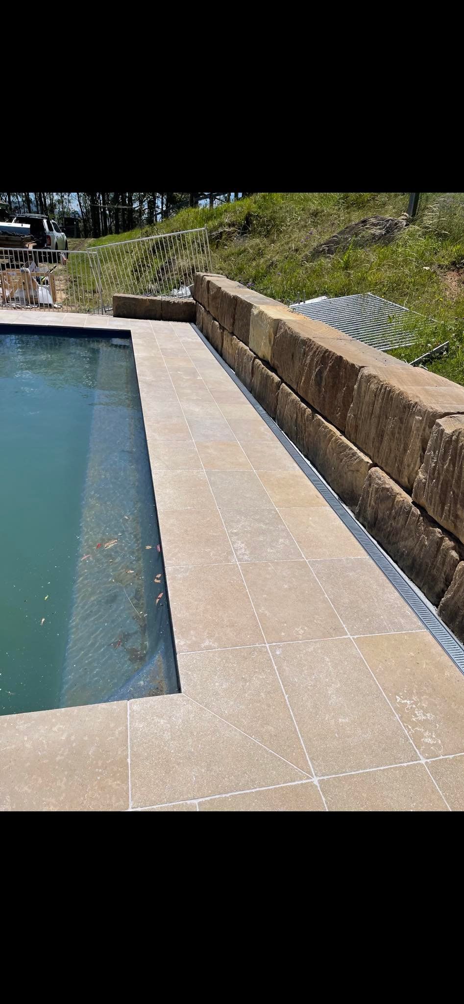 A rectangular swimming pool with a concrete border next to a stone retaining wall. — East Coast Paving in Seaham, NSW