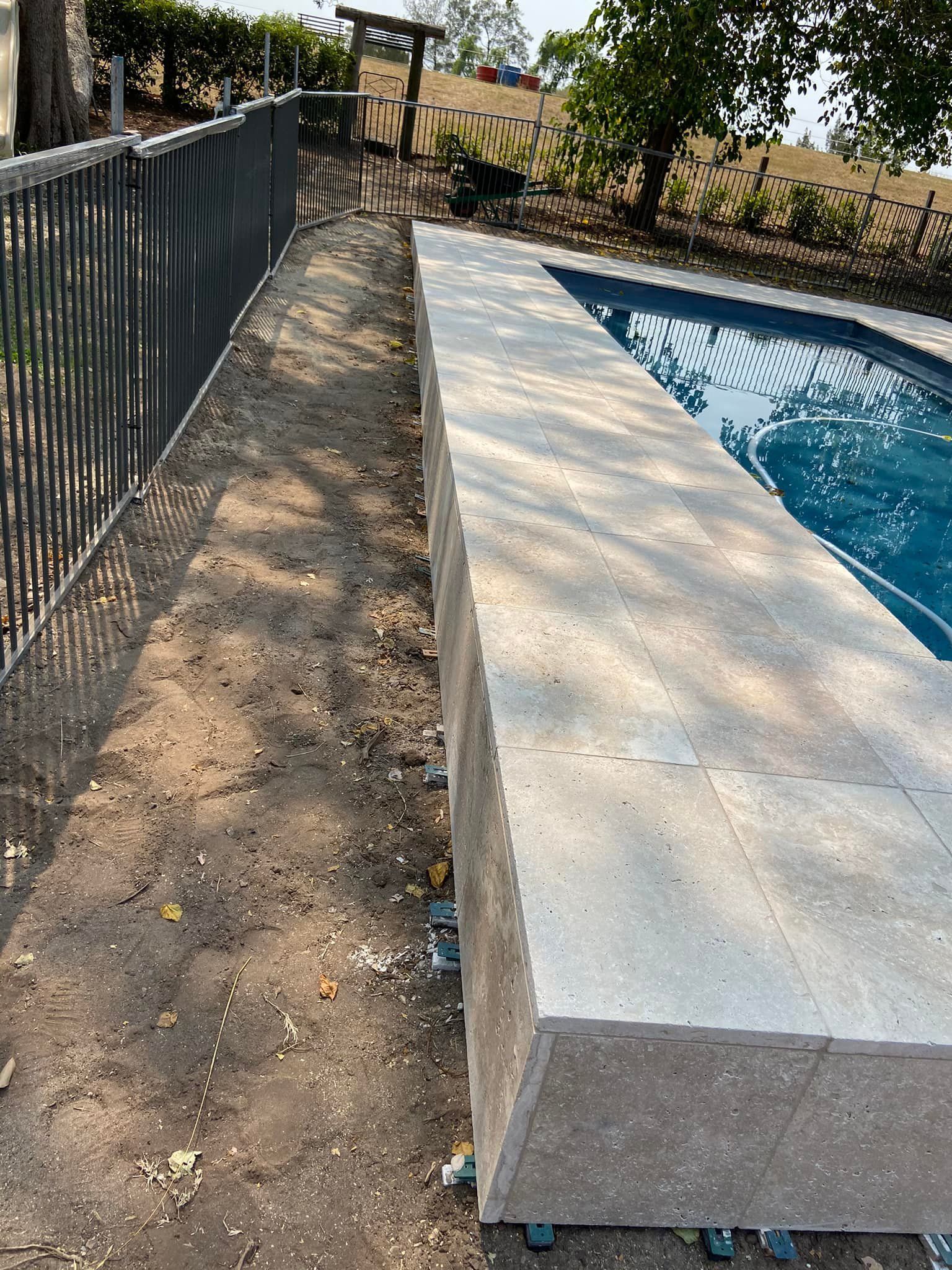 Poolside stone ledge next to a fence and bare earth. — East Coast Paving in Seaham, NSW