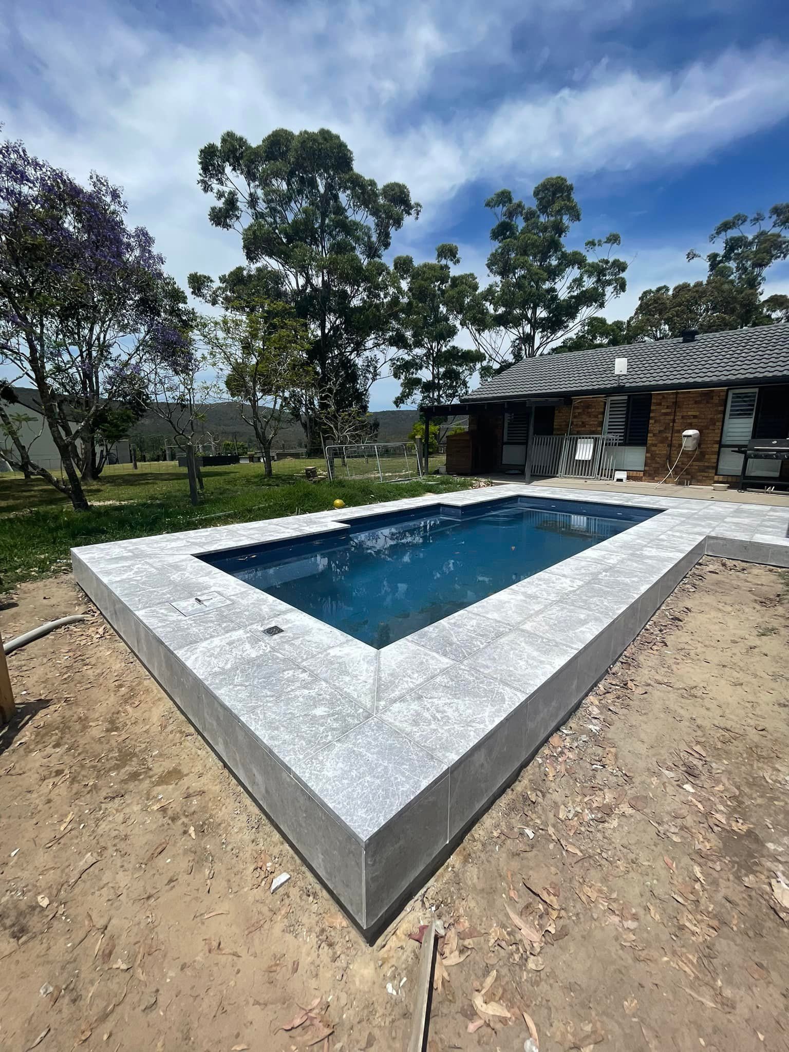 Rectangular pool with gray concrete edging, set in a yard, under a blue sky. — East Coast Paving in Seaham, NSW