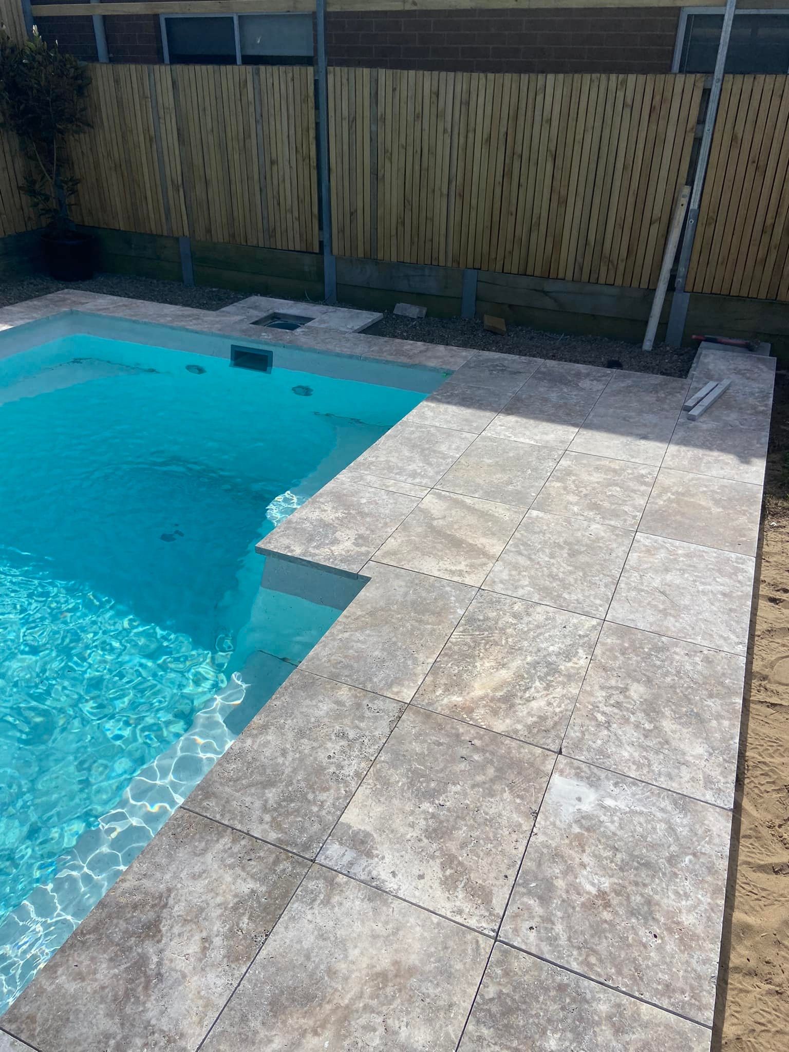 Swimming pool with travertine tile coping and surround; wood fence in background. — East Coast Paving in Seaham, NSW