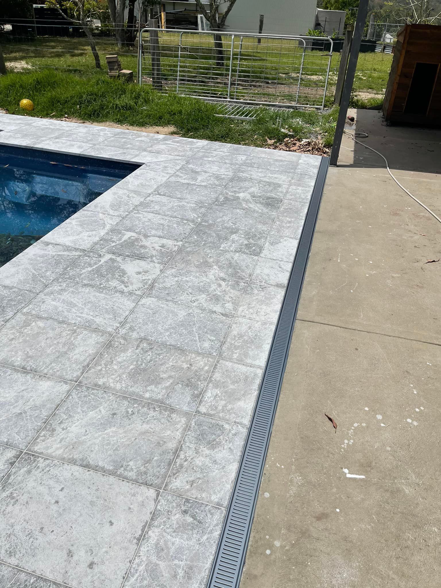 Poolside patio with gray pavers and a blue pool next to a concrete walkway. — East Coast Paving in Seaham, NSW