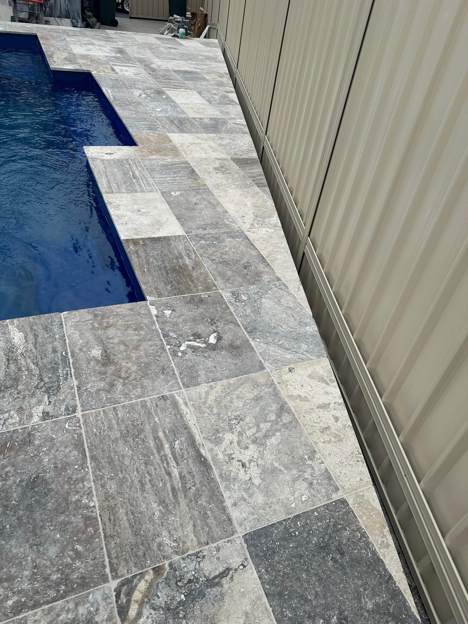 Poolside patio with gray stone tiles next to a blue pool and a cream-colored fence. — East Coast Paving in Seaham, NSW