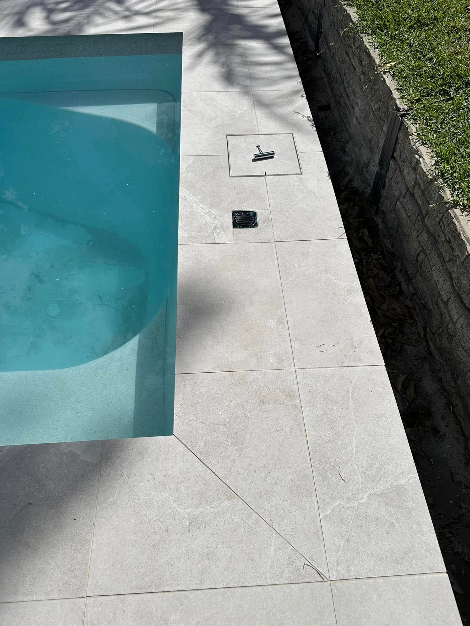 Pool's edge with light blue water, grey stone tiles, and a grass border. — East Coast Paving in Seaham, NSW