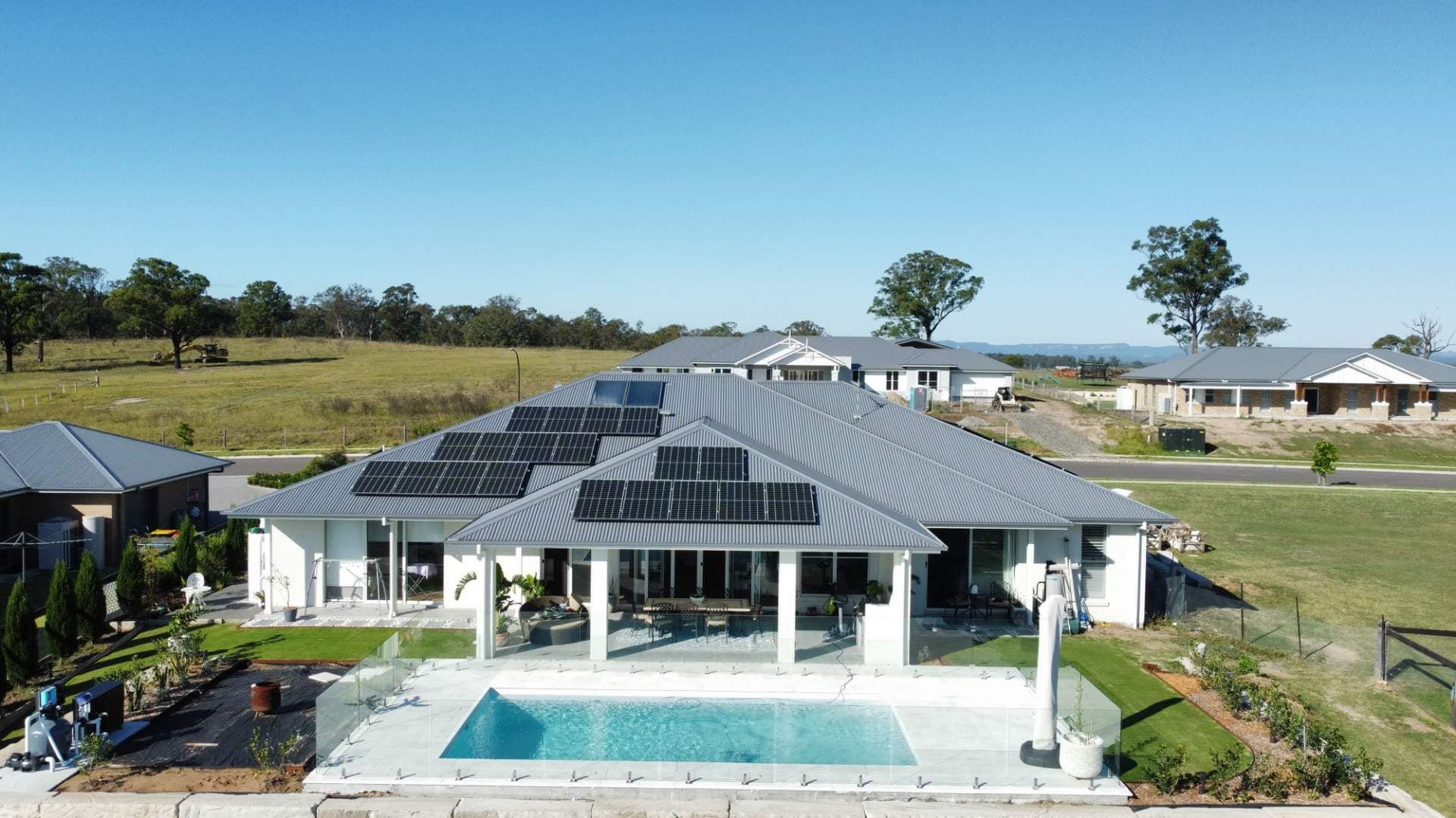 Large white house with solar panels on the roof, pool, and green lawn on a sunny day. — East Coast Paving in Seaham, NSW