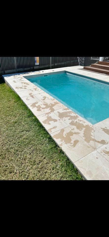 A rectangular swimming pool surrounded by light-colored stone and green grass.