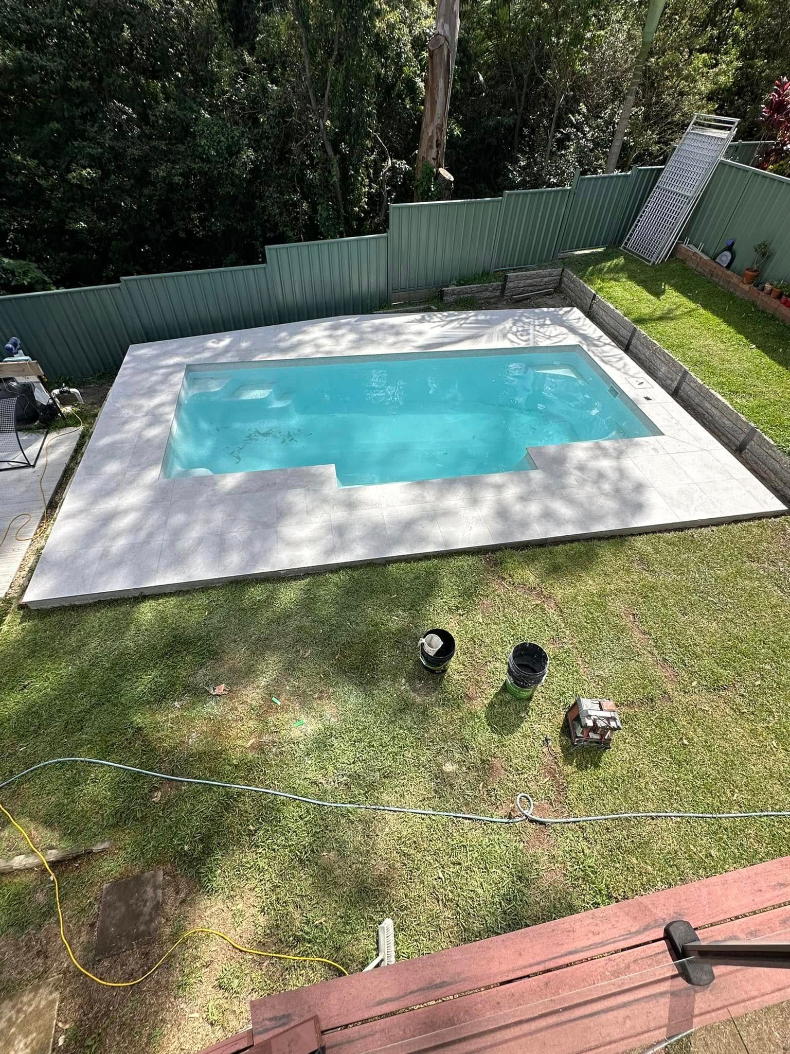 Swimming pool with light blue water, concrete border, and surrounding green grass. — East Coast Paving in Seaham, NSW