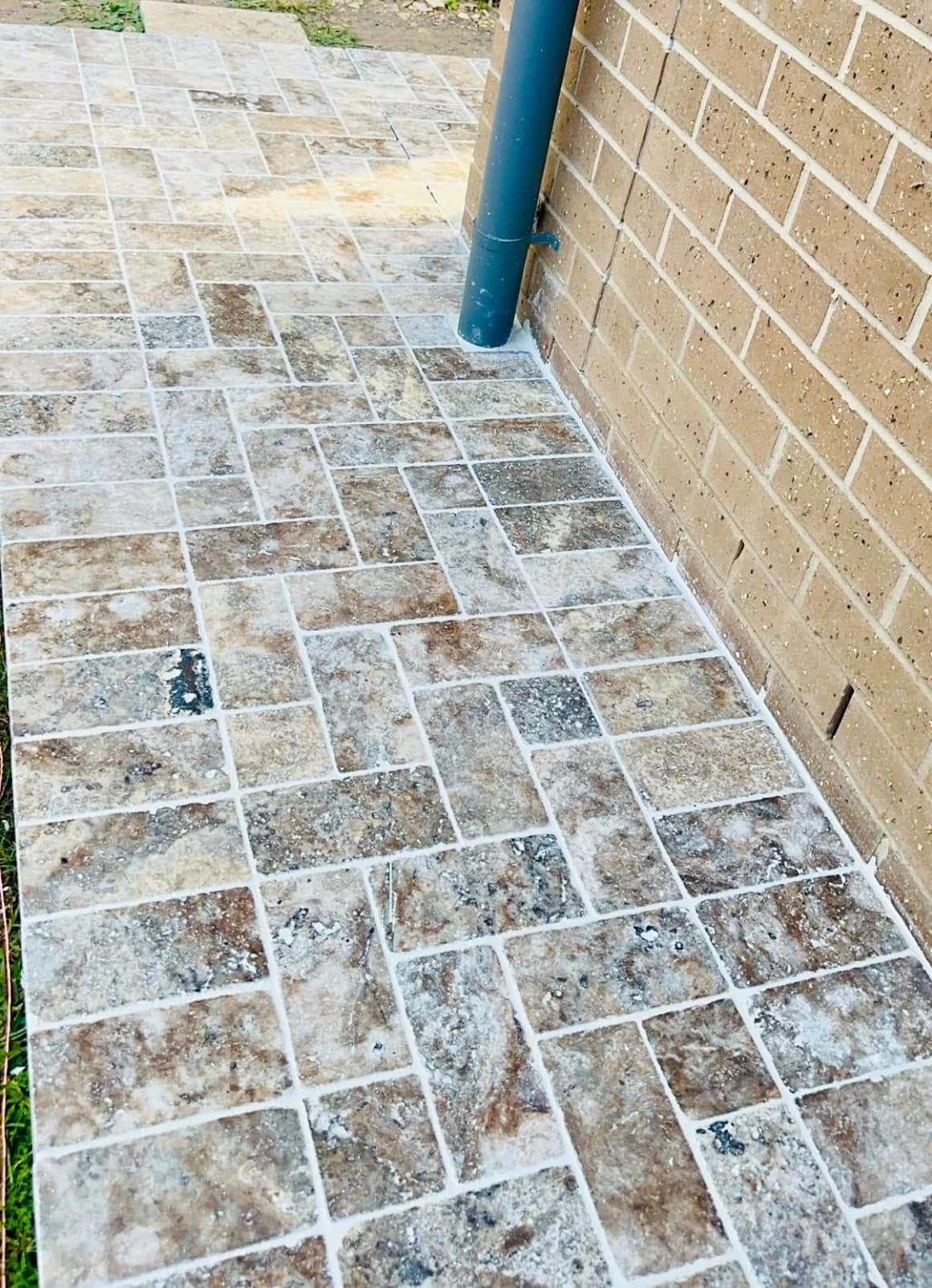 Stone tile walkway next to a brick wall and a downspout, tiles are brown, beige, and gray. — East Coast Paving in Seaham, NSW
