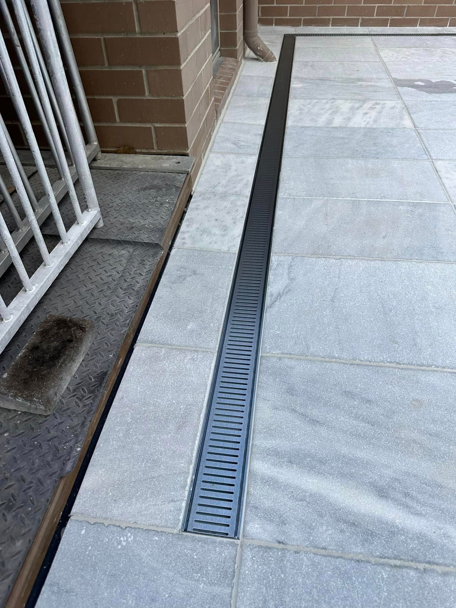 Gray tiled patio with a linear drain next to a brick wall. — East Coast Paving in Seaham, NSW