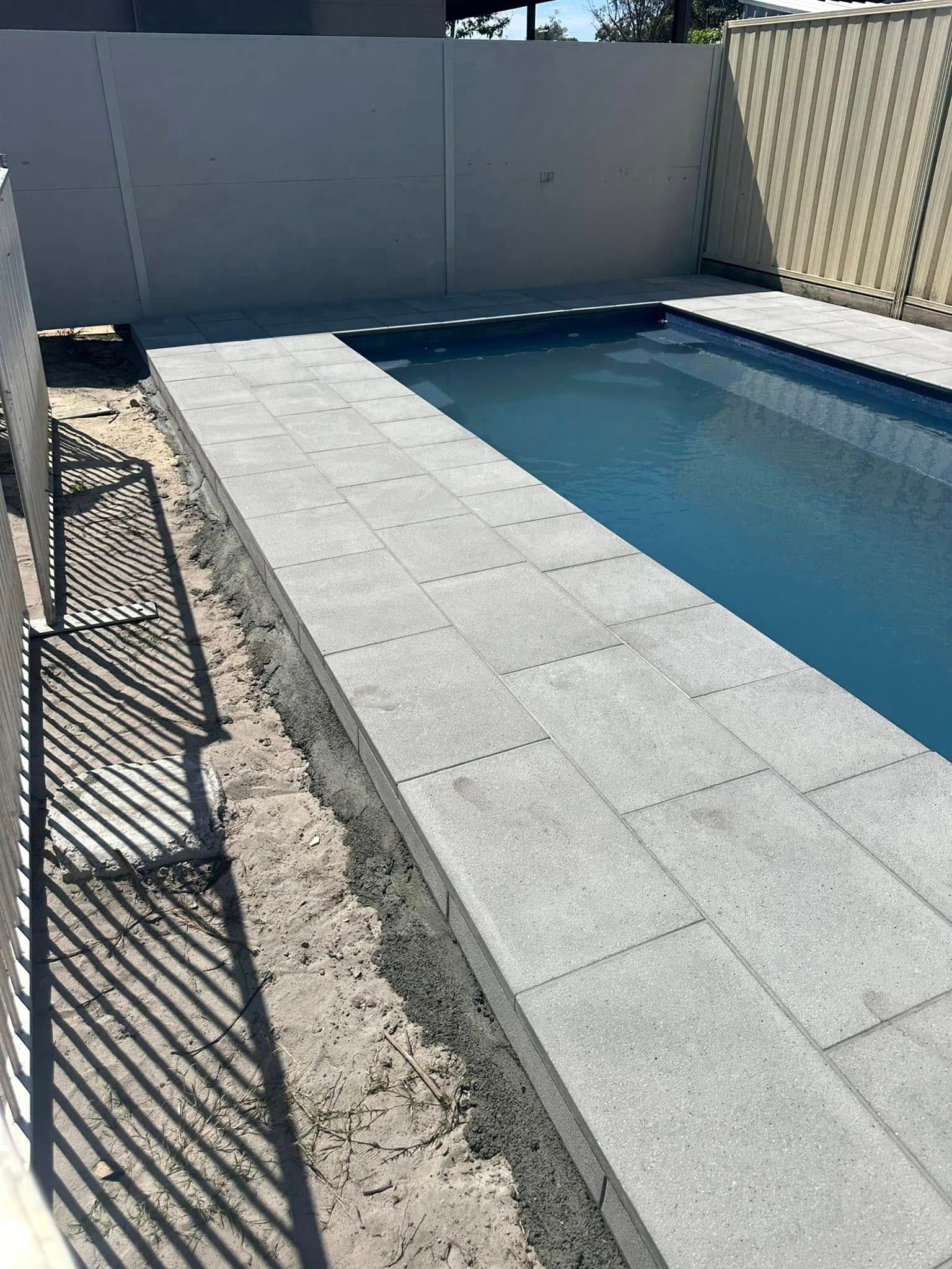 Poolside with gray pavers and water, next to a fence and wall. — East Coast Paving in Seaham, NSW