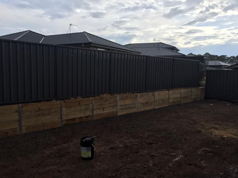 Wooden retaining wall below a dark gray corrugated fence. Backyard setting. — East Coast Paving in Seaham, NSW