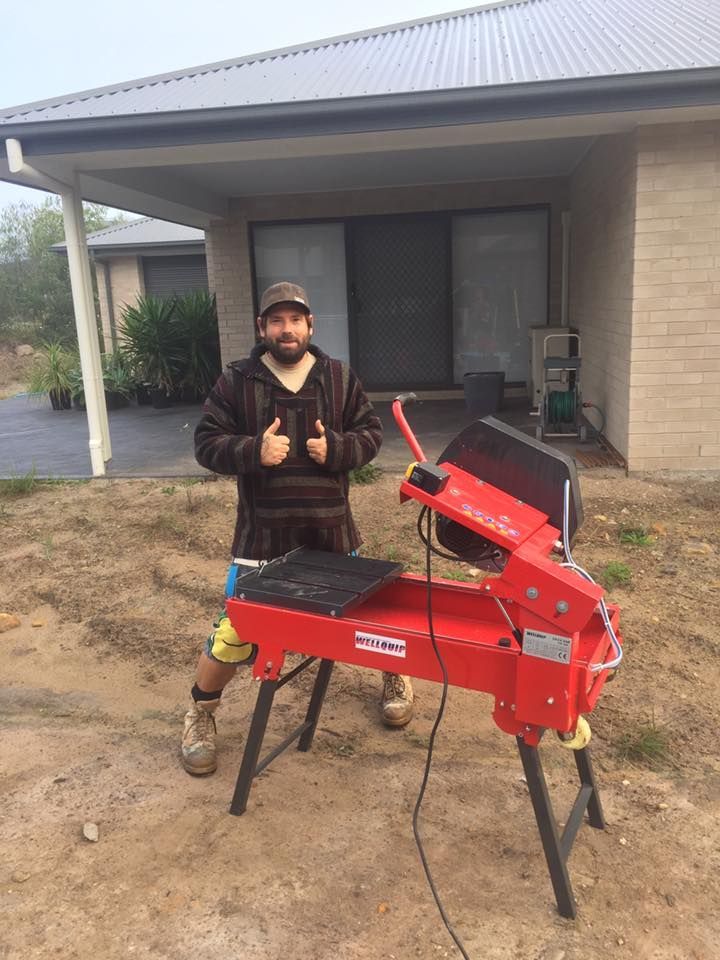 Man giving thumbs-up next to a red tile saw, outside a house. — East Coast Paving in Seaham, NSW