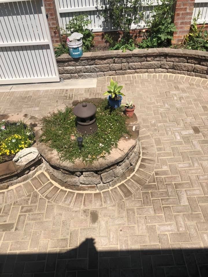 Brick patio with circular brick planter, surrounding stonewall, and white fence in the background. — East Coast Paving in Seaham, NSW