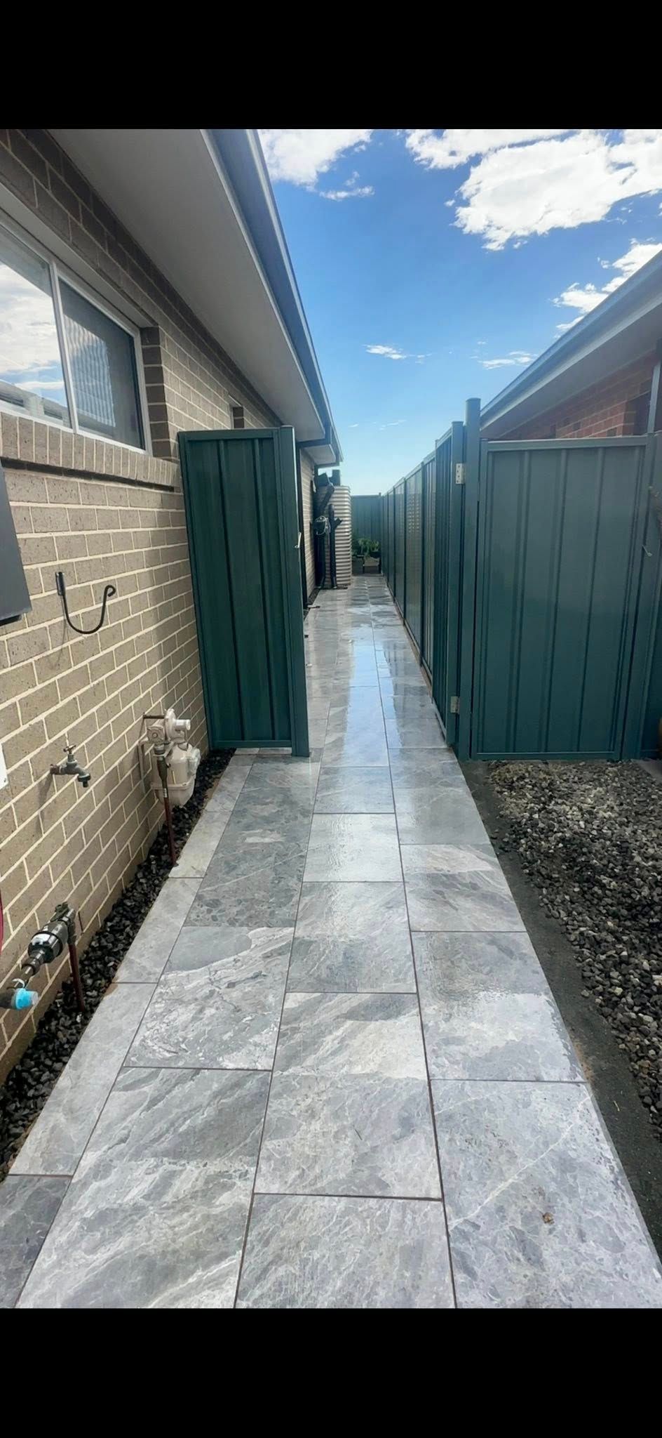 A narrow paved walkway between buildings, bordered by a fence and brick wall, with a blue sky visible. — East Coast Paving in Seaham, NSW